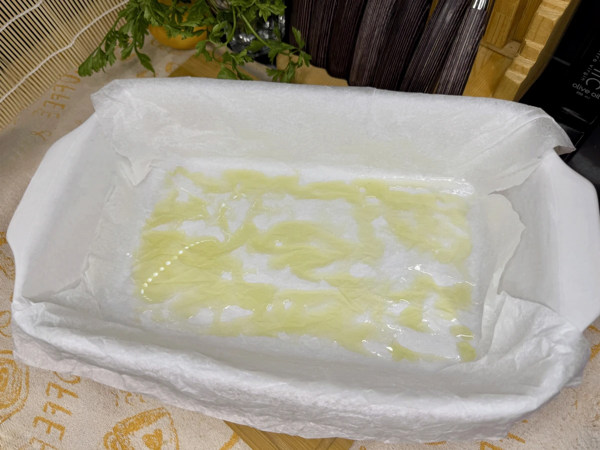 Pleh sa papirom za pečenje i uljem, spreman za pečenje pohovanog oslića u rerni.