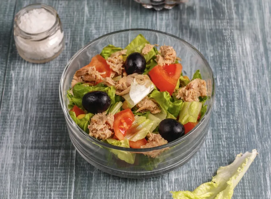 Zelena salata sa tunjevinom, uz dodatak paradajza i crnih maslina, servirana u providnoj činiji.