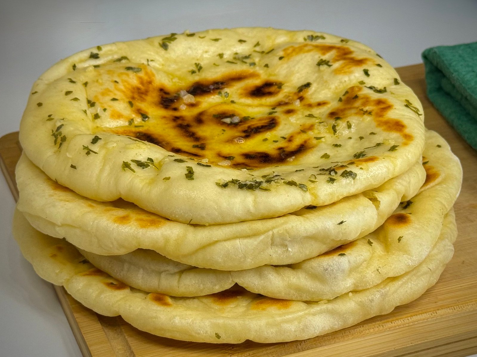 Indijske naan lepinje sa premazom od maslaca, bijelog luka i začina, naslagane jedna na drugu, na drvenoj dasci.