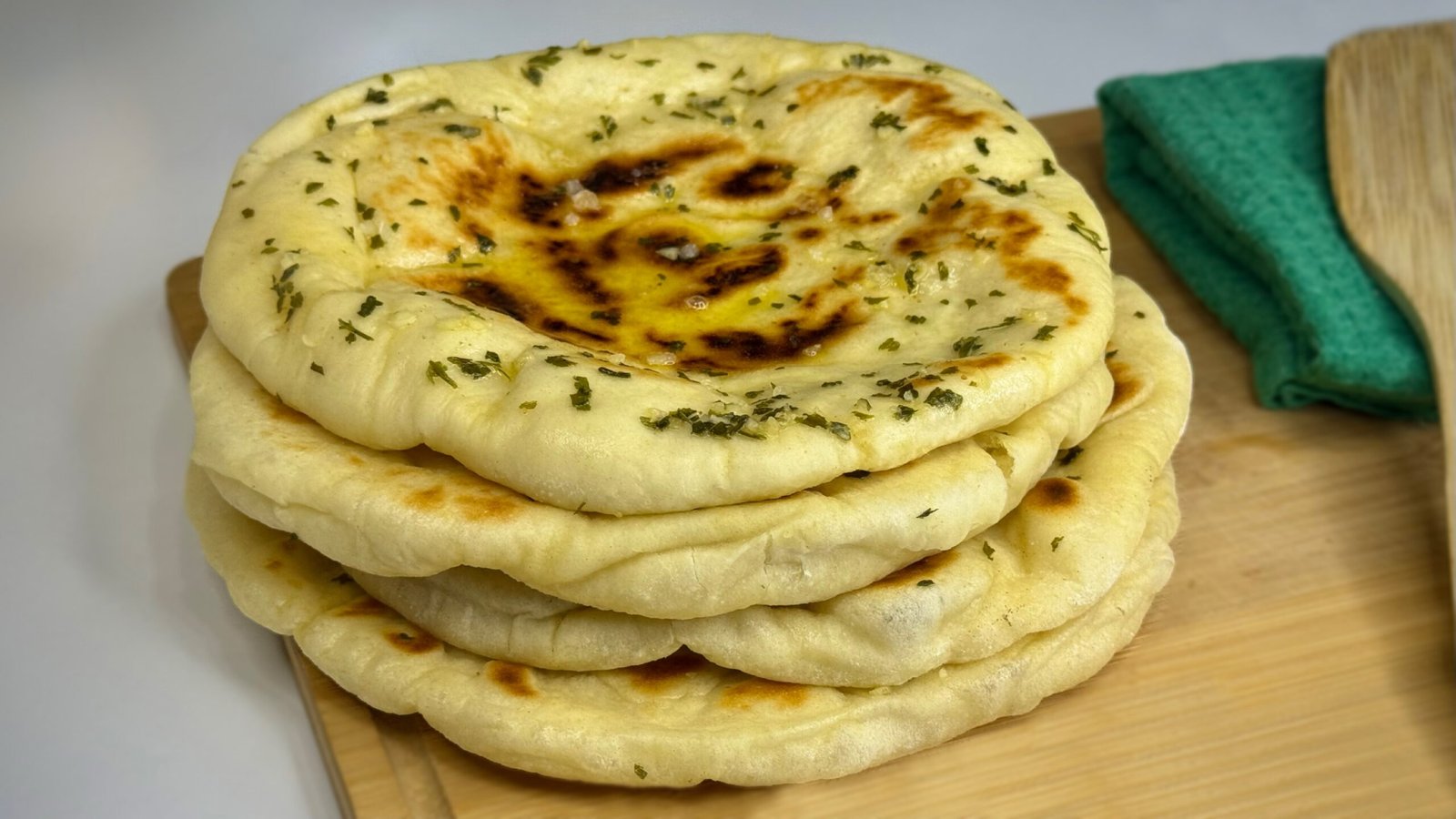 Indijske naan lepinje sa premazom od maslaca, bijelog luka i začina, naslagane jedna na drugu, na drvenoj dasci.
