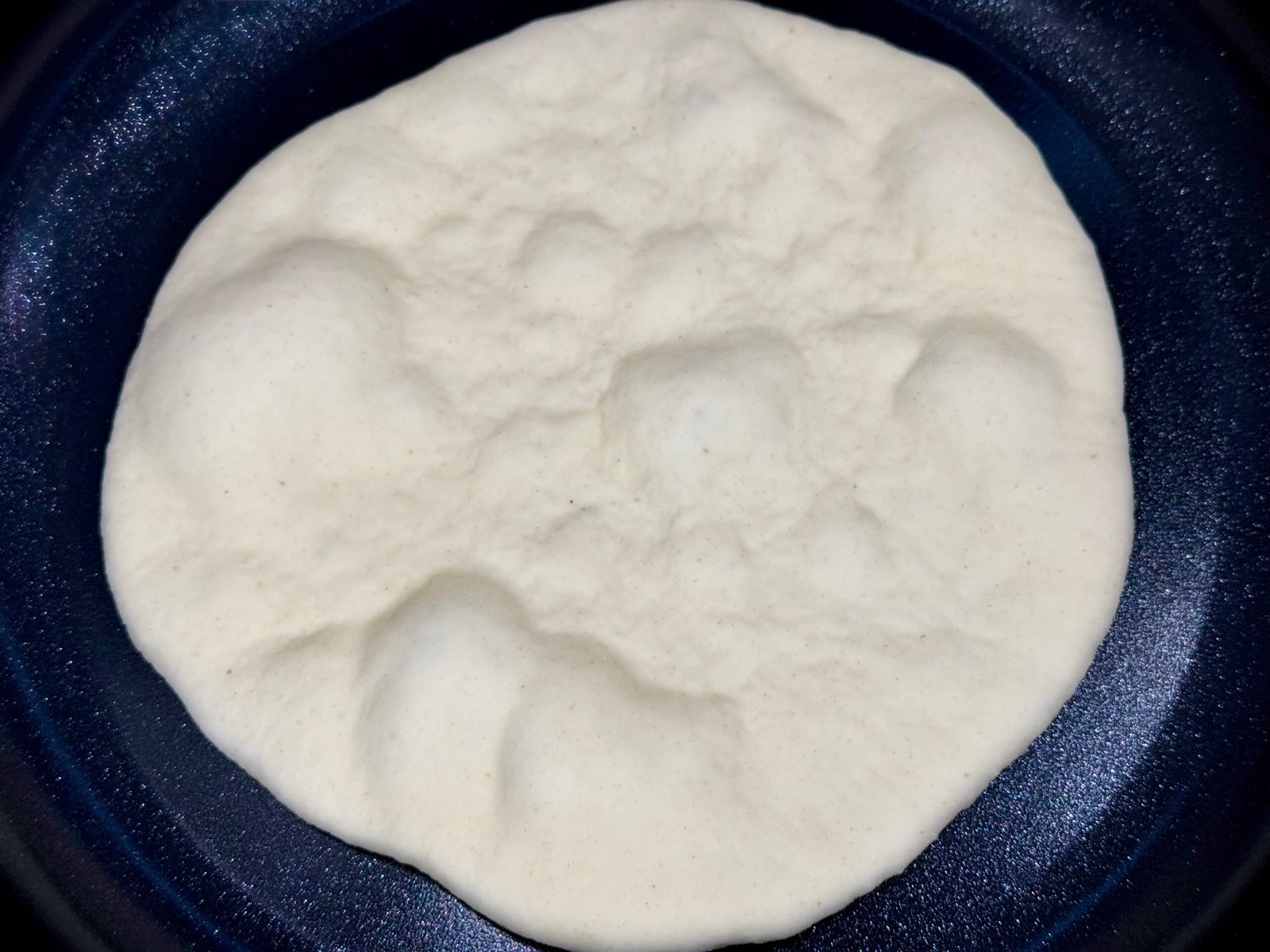 Pečenje naan lepinje na tavi, mjehurići na površini tijesta.