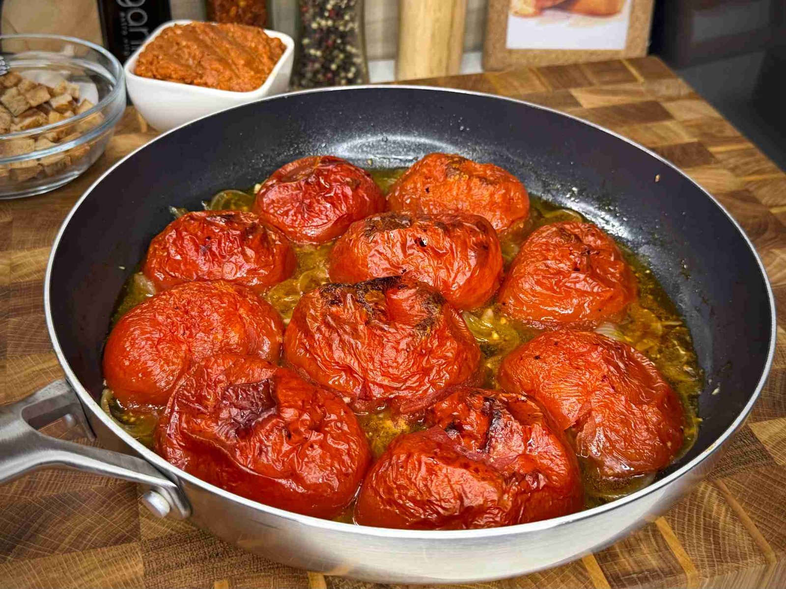 Pečeni paradajz iz rerne, serviran u tavi na drvenoj dasci.