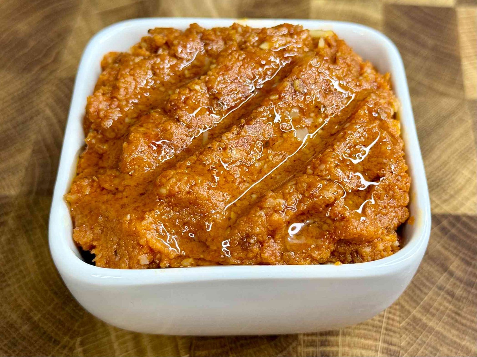 Pesto od sušenog paradajza i parmezana, serviran u bijeloj činiji na drvenoj dasci.