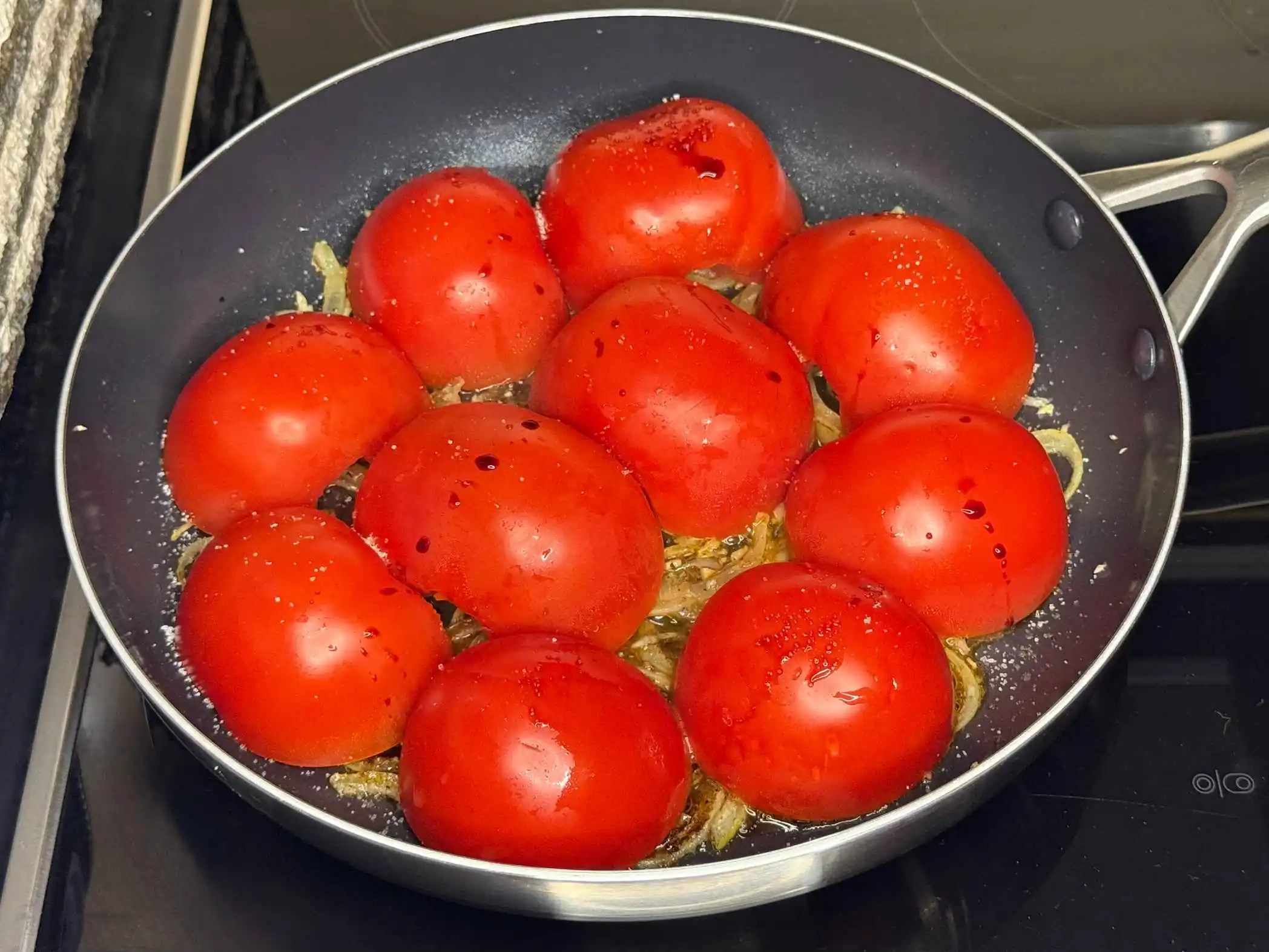 Prženje polovina paradajza na tavi, sa crvenim lukom.