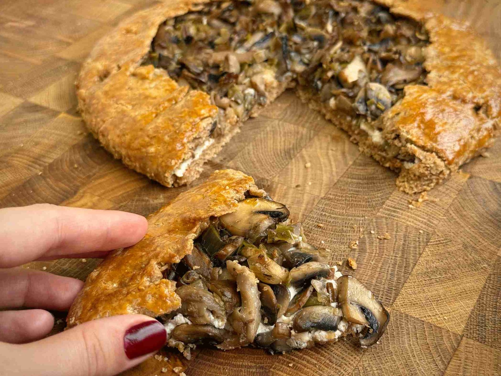Parče galette sa gljivama i rikotom na drvenoj dasci, pečena do zlatne, hrskave korice.