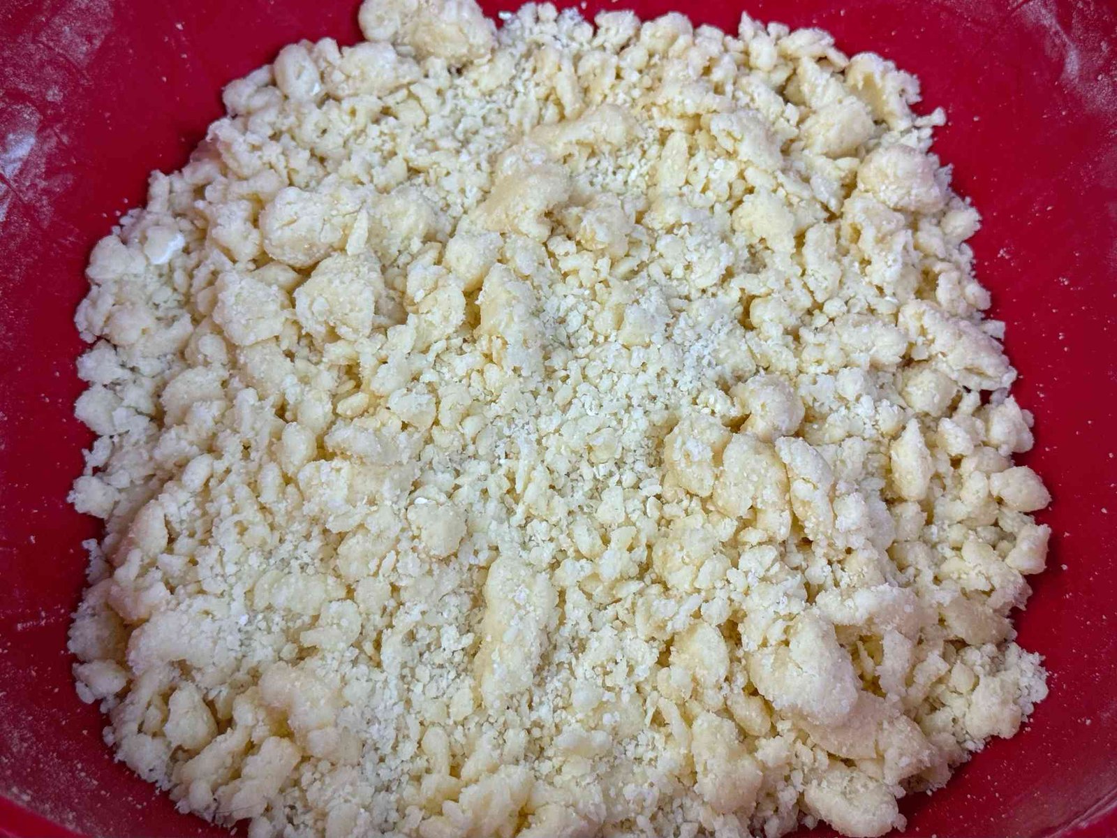 Mrvičasto prhko tijesto za tart od jabuka u crvenoj posudi, napravljeno od maslaca i brašna.