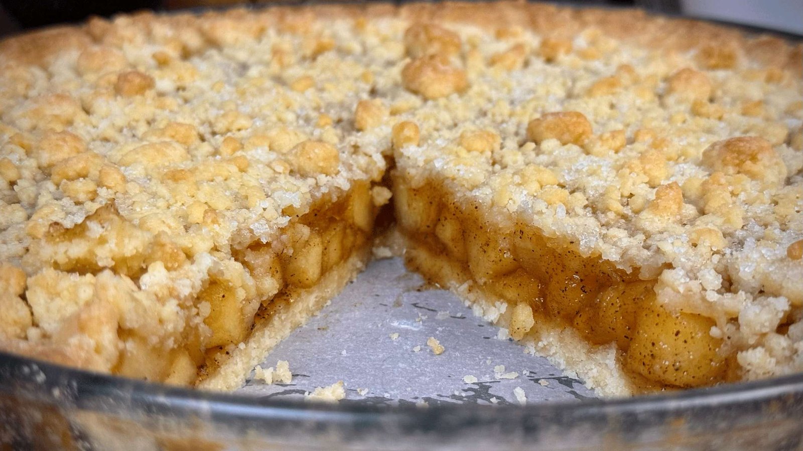 Cijeli tart od jabuka u kalupu sa isječenom kriškom, prikazuje bogat fil i hrskavu, mrvičastu koricu.