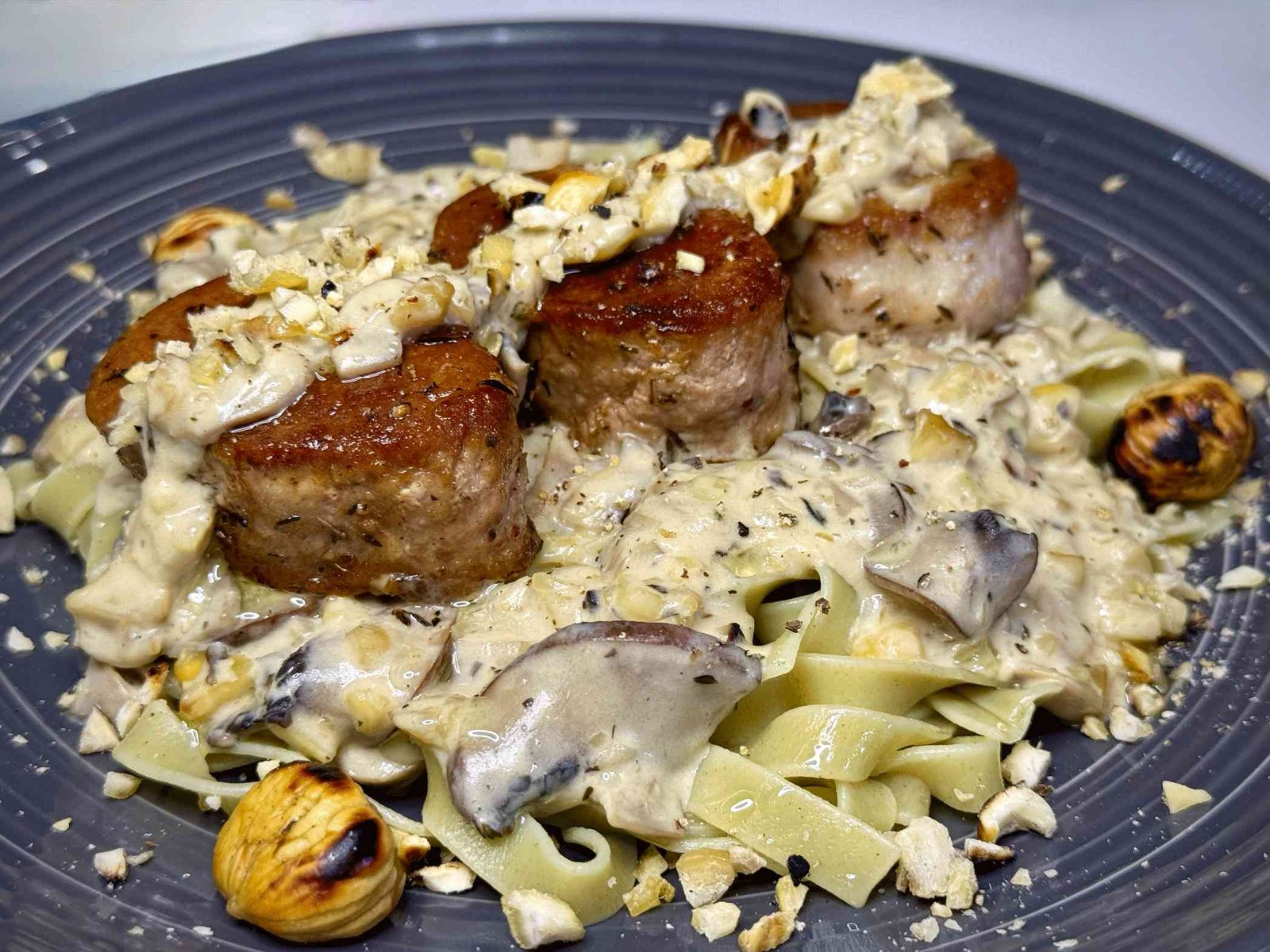 svinjski-file-u-sosu-od-gljiva Svinjski file u kremastom sosu od gljiva i kestena, serviran na tanjiru preko taljatela. File je sočan sa zlatnom koricom.