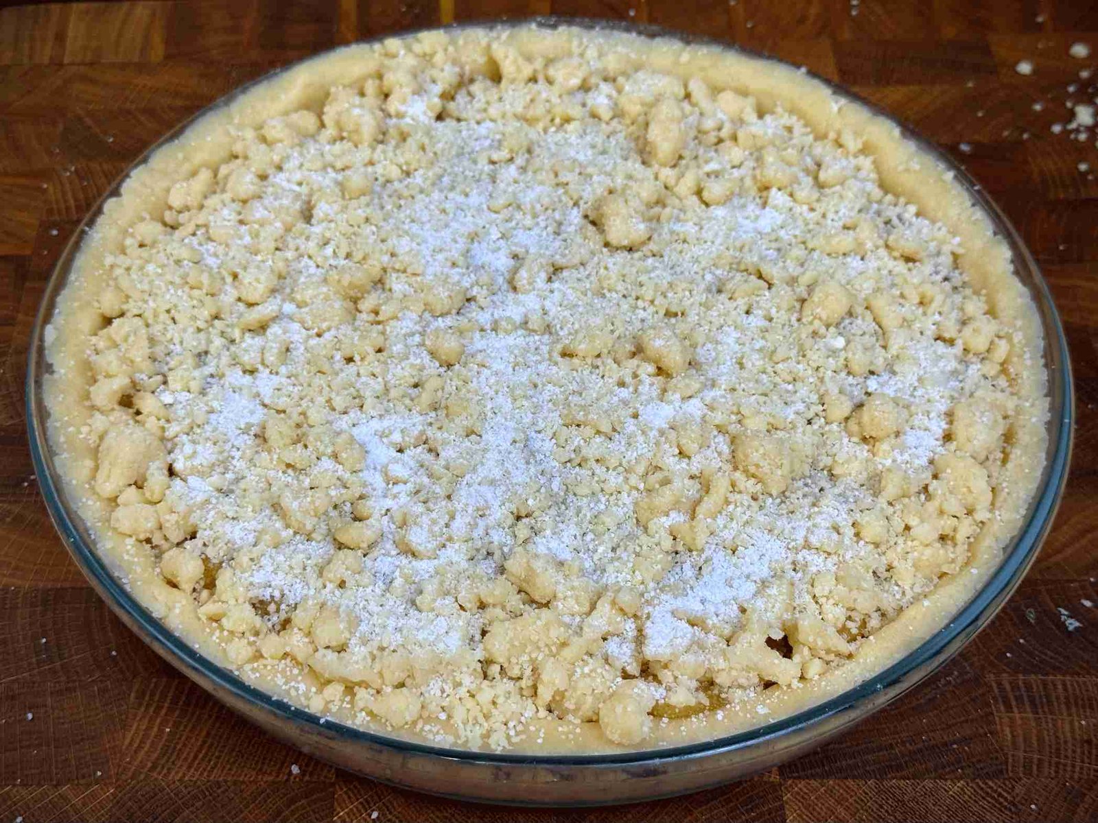 Sirovi tart od jabuka u staklenom kalupu, posut mrvičastim tijestom i šećerom, spreman za rernu.