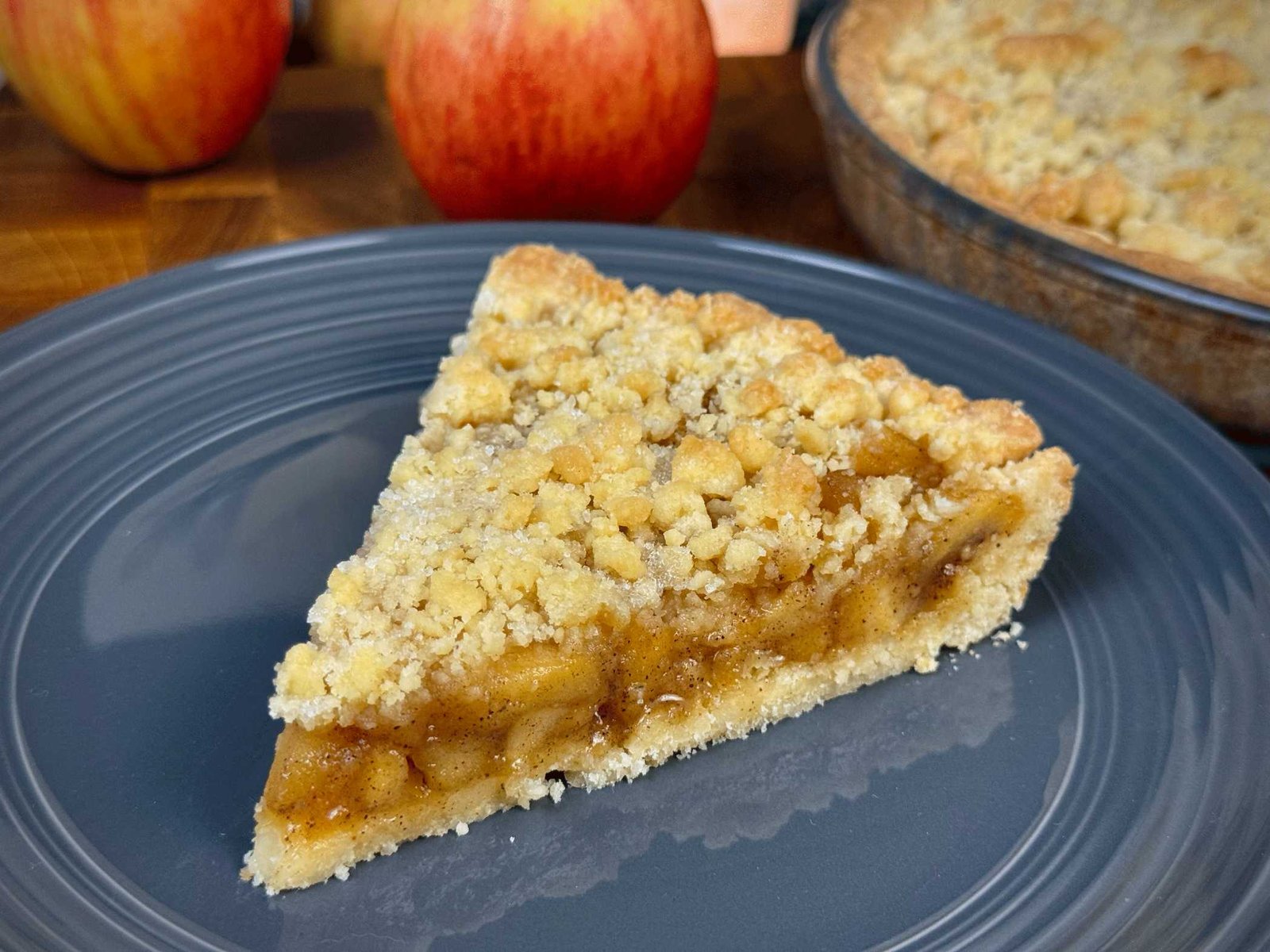 Kriška tarta od jabuka sa mrvičastim tijestom i sočnim filom od karamelizovanih jabuka, servirana na sivom tanjiru.