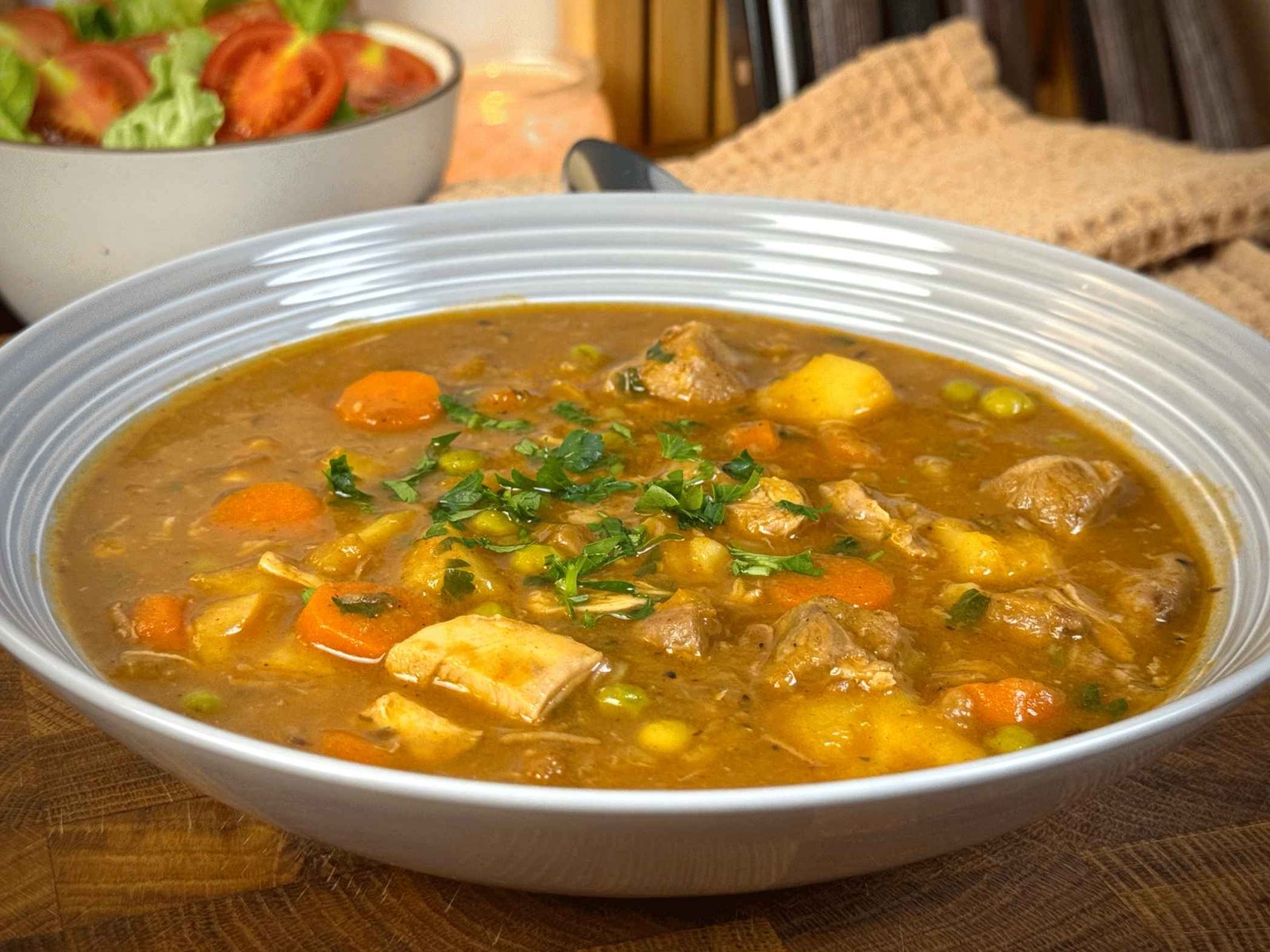 Zdjela bogate čorbe sa tri vrste mesa i povrćem, posuta svježim peršunom, servirana uz salatu u pozadini.