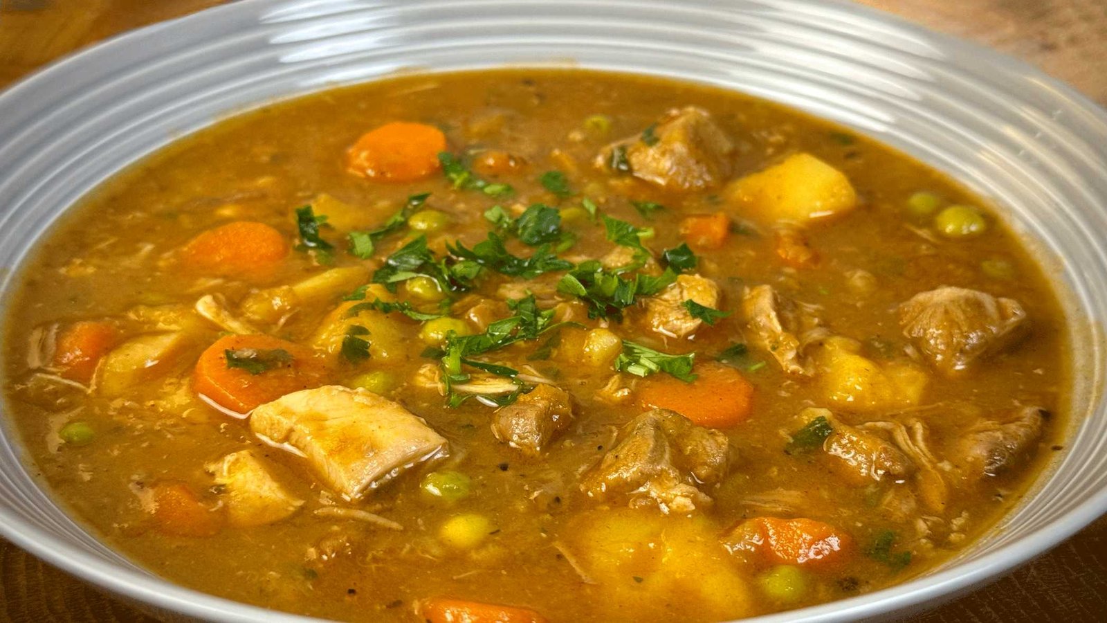 corba-tri-vrste-mesa Zdjela bogate čorbe sa tri vrste mesa i povrćem, posuta svježim peršunom, servirana uz salatu u pozadini.