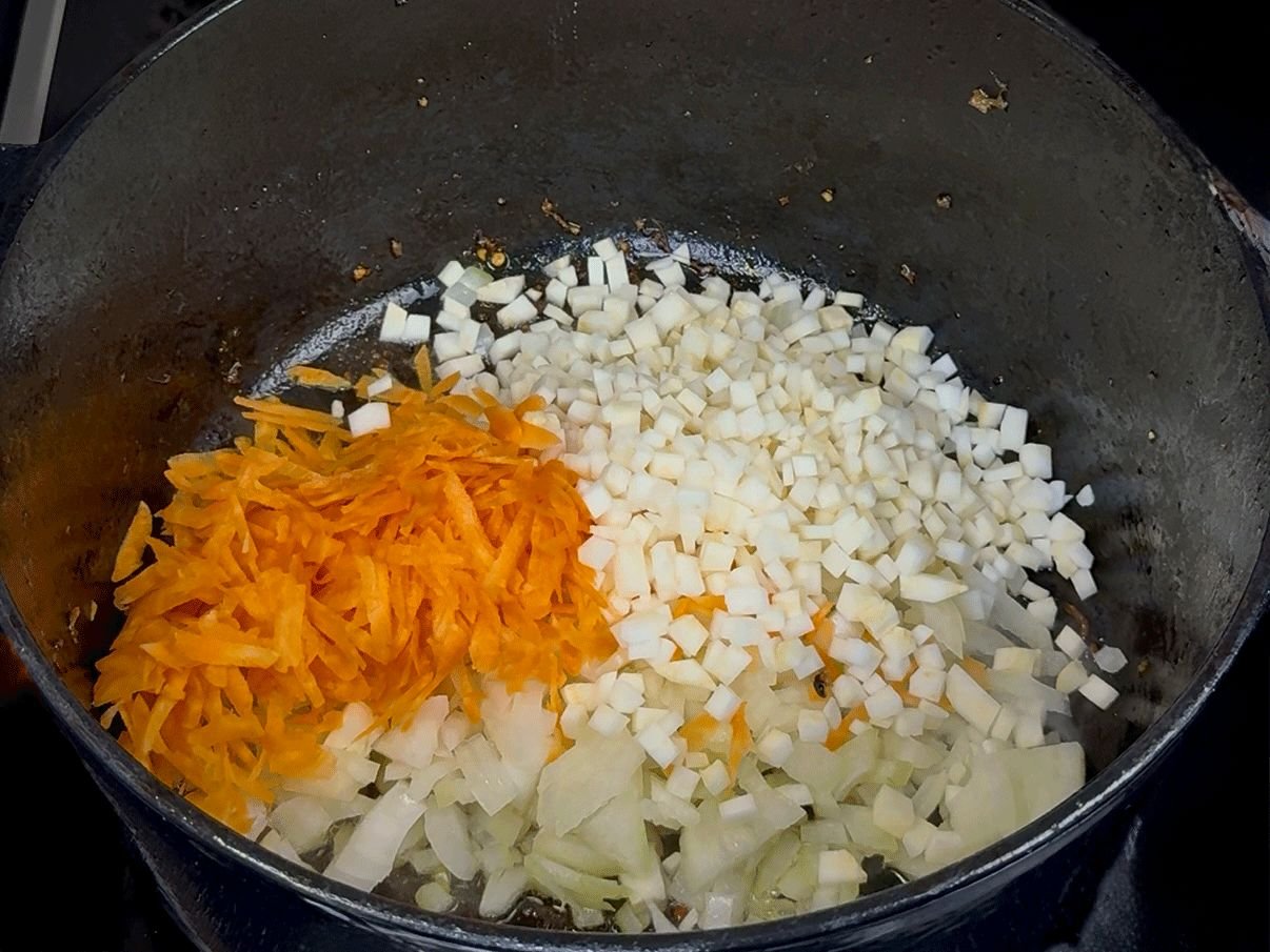 Dinstanje aromatične baze za čorbu u crnom loncu: sjeckani crni luk, celer i narendana mrkva.