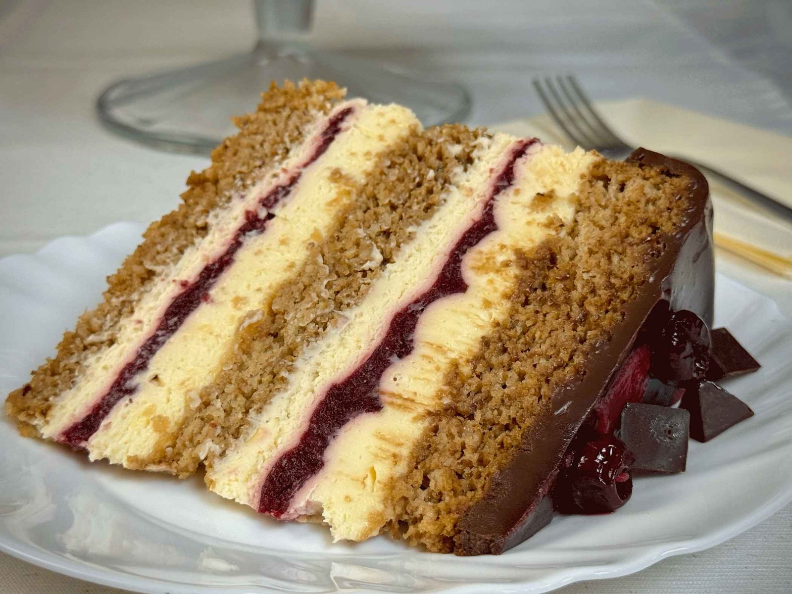 Detaljan prikaz sočnog komada Moka Amarena torte na bijelom tanjiru, sa vidljivim slojevima kore od oraha, mascarpone fila i fila od višanja.