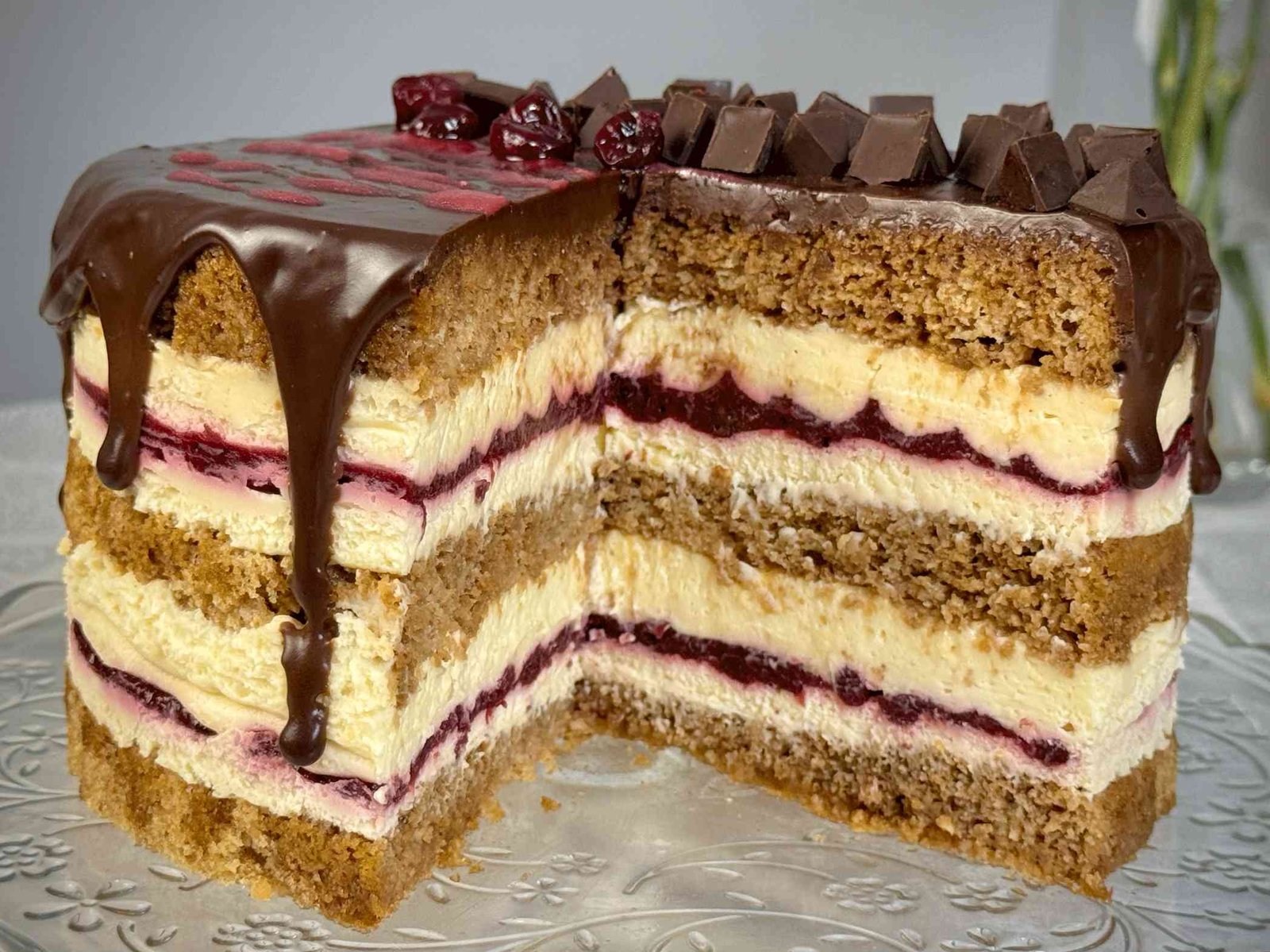 Presjek Moka Amarena torte sa jasno vidljivim slojevima kore, bijelog mascarpone fila i crvenog fila od višanja, na staklenom postolju.