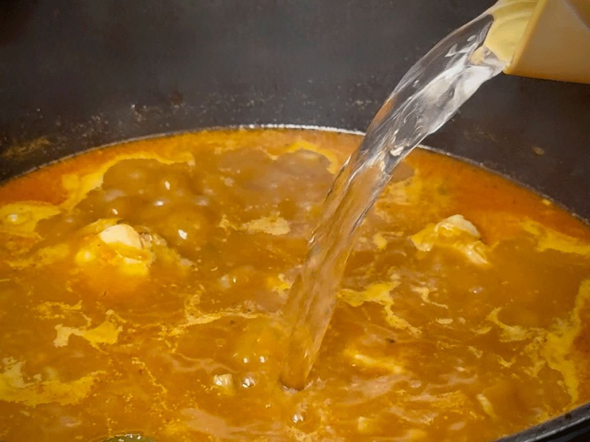 Nalivanje vode ili temeljca u lonac preko baze od paradajza i mesa za početak kuhanja čorbe.