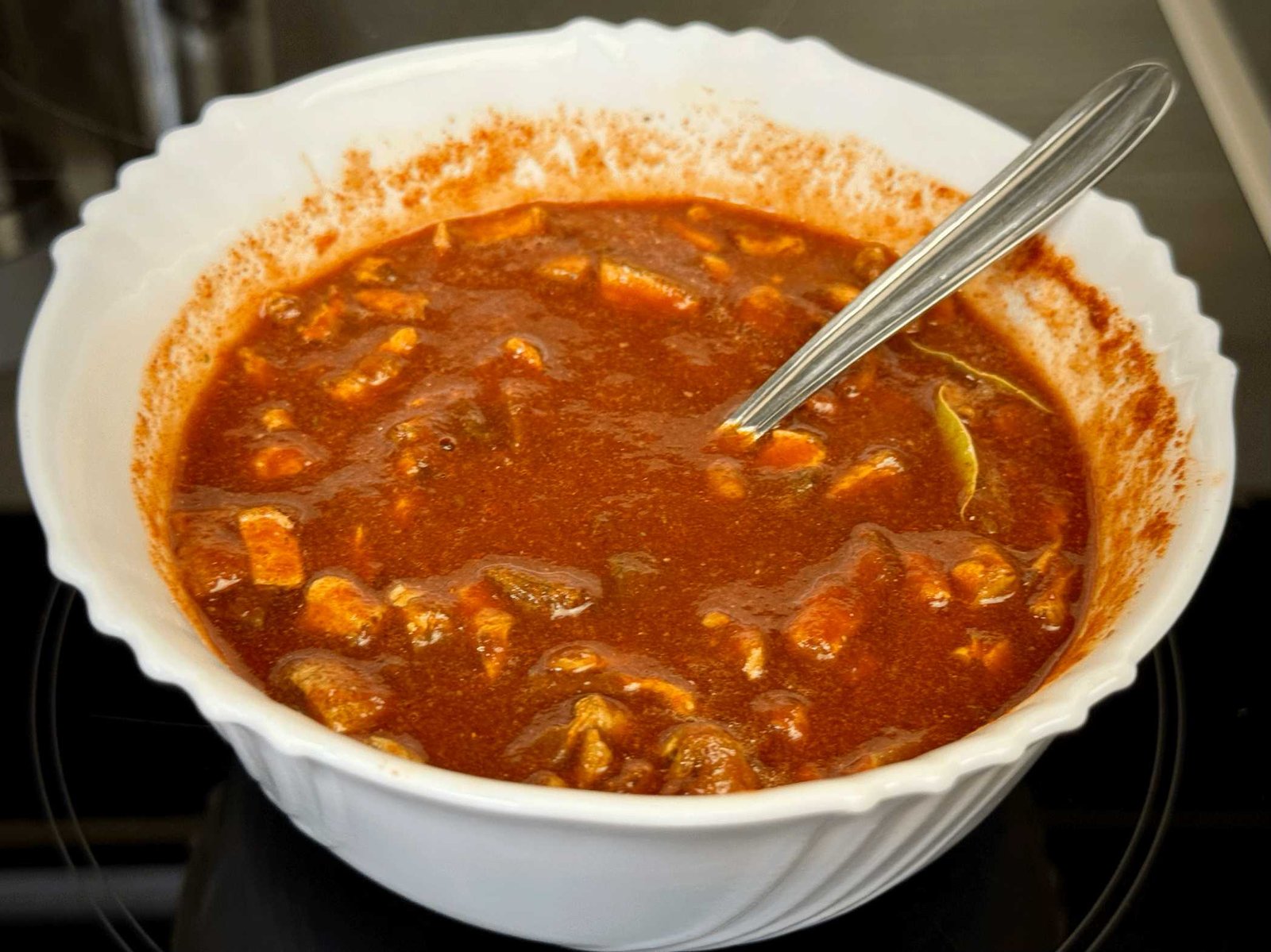 Pasirani paradajz pomiješan sa crvenom paprikom, vrganjima i lovorovim listom u bijeloj zdjeli.