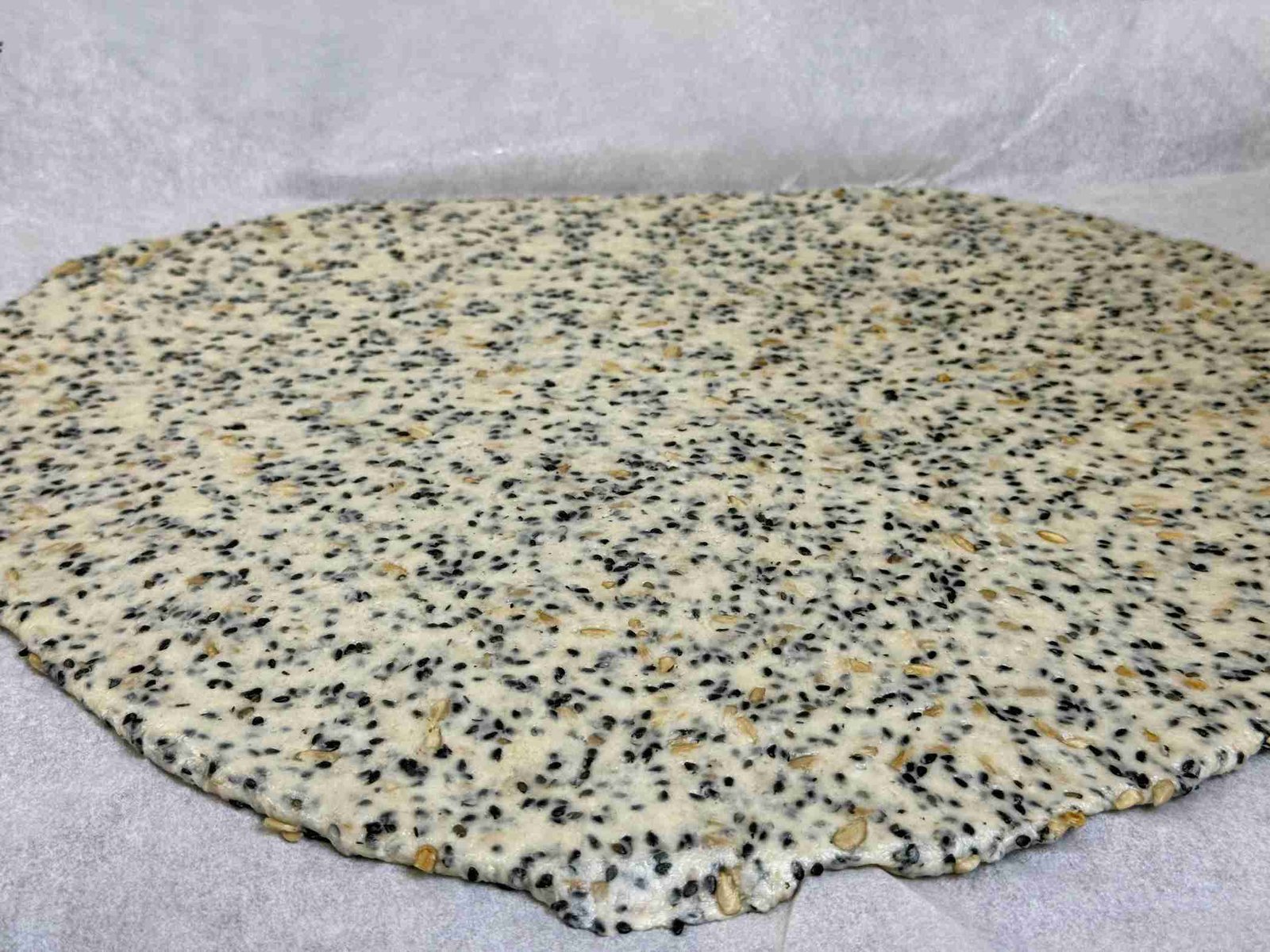 Razvijeno posno tijesto sa crnim susamom i suncokretom između dva pek papira.