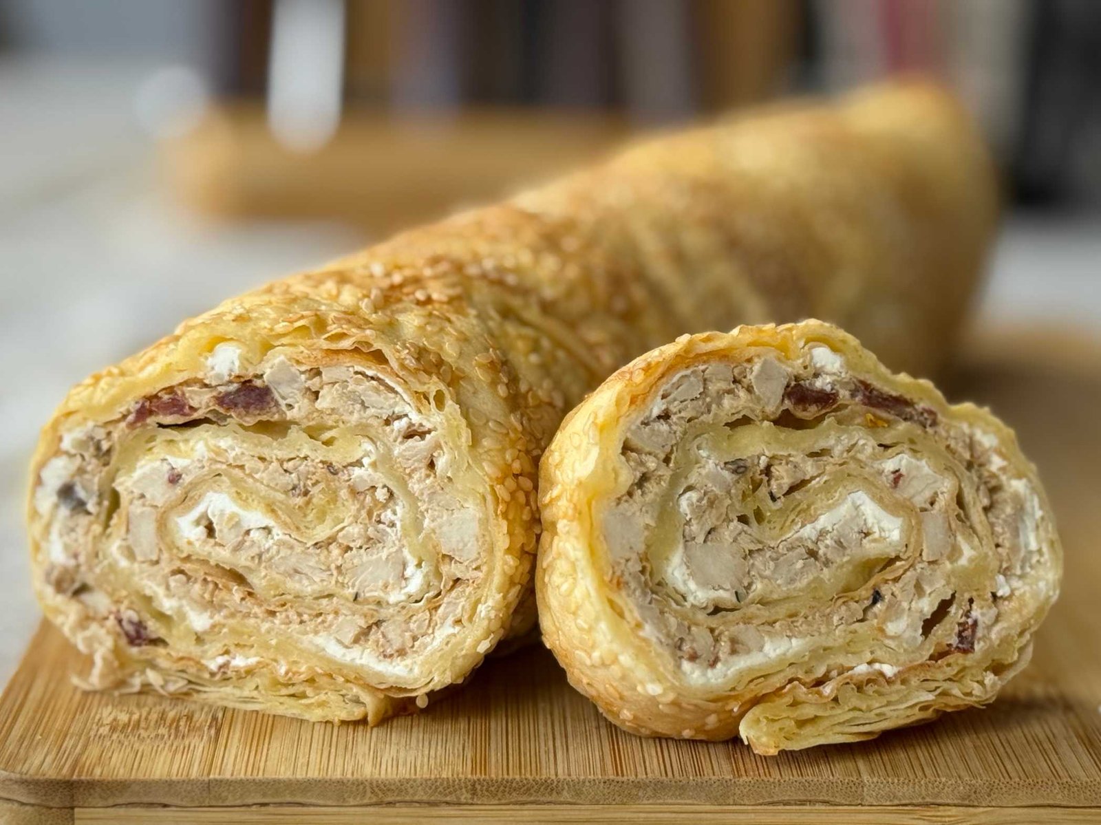 Slani rolat od gotovih kora sa kremastim filom od piletine i sušenog paradajza, posut susamom, serviran na drvenoj dasci.