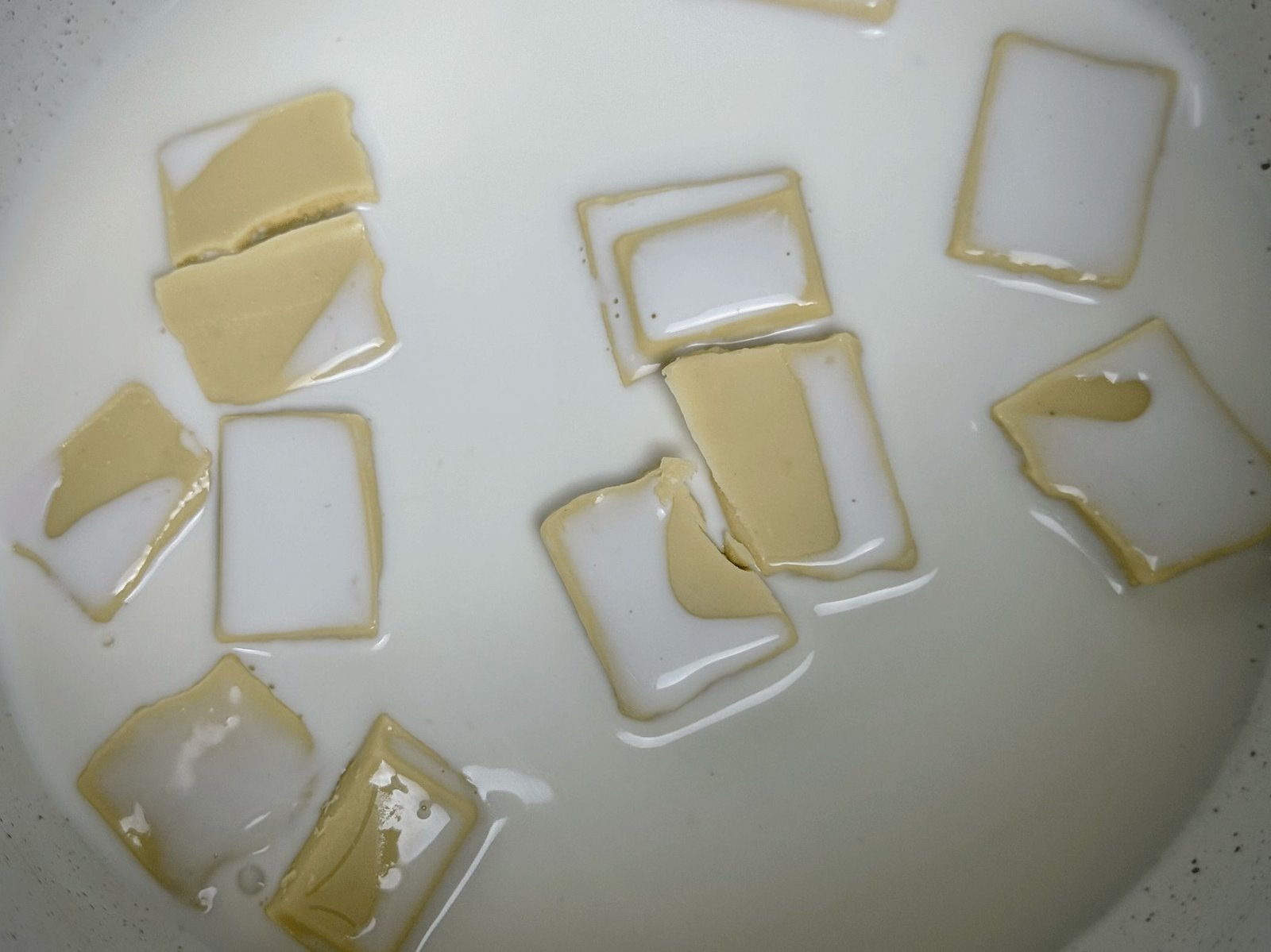 Kockice posne bijele čokolade potopljene u posnu slatku pavlaku u šerpi - bijeli ganaš.