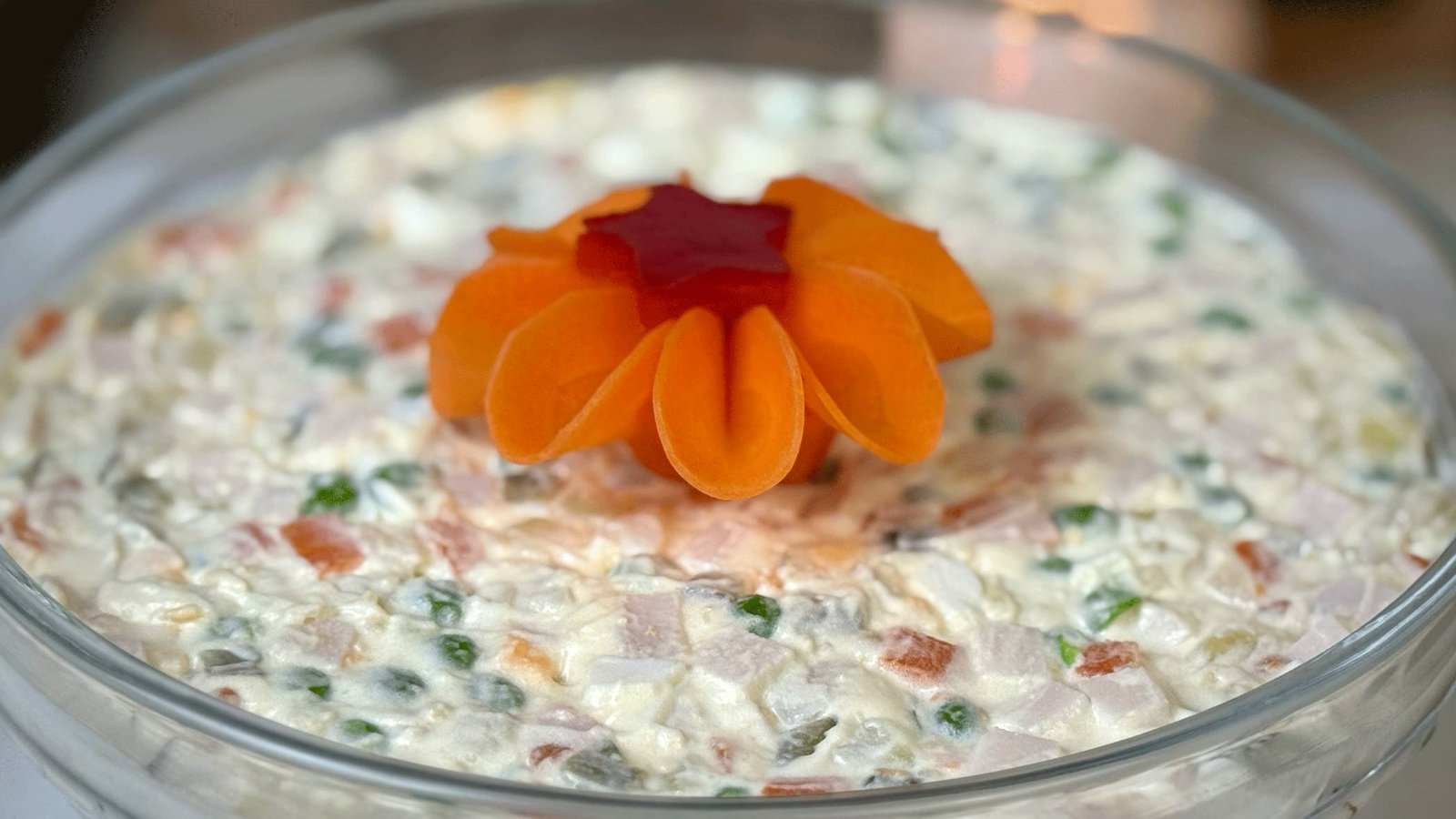 Kremasta ruska salata servirana u staklenoj činiji, sa savršeno sitno sjeckanim sastojcima i dekorativnim cvijetom od mrkve na vrhu.