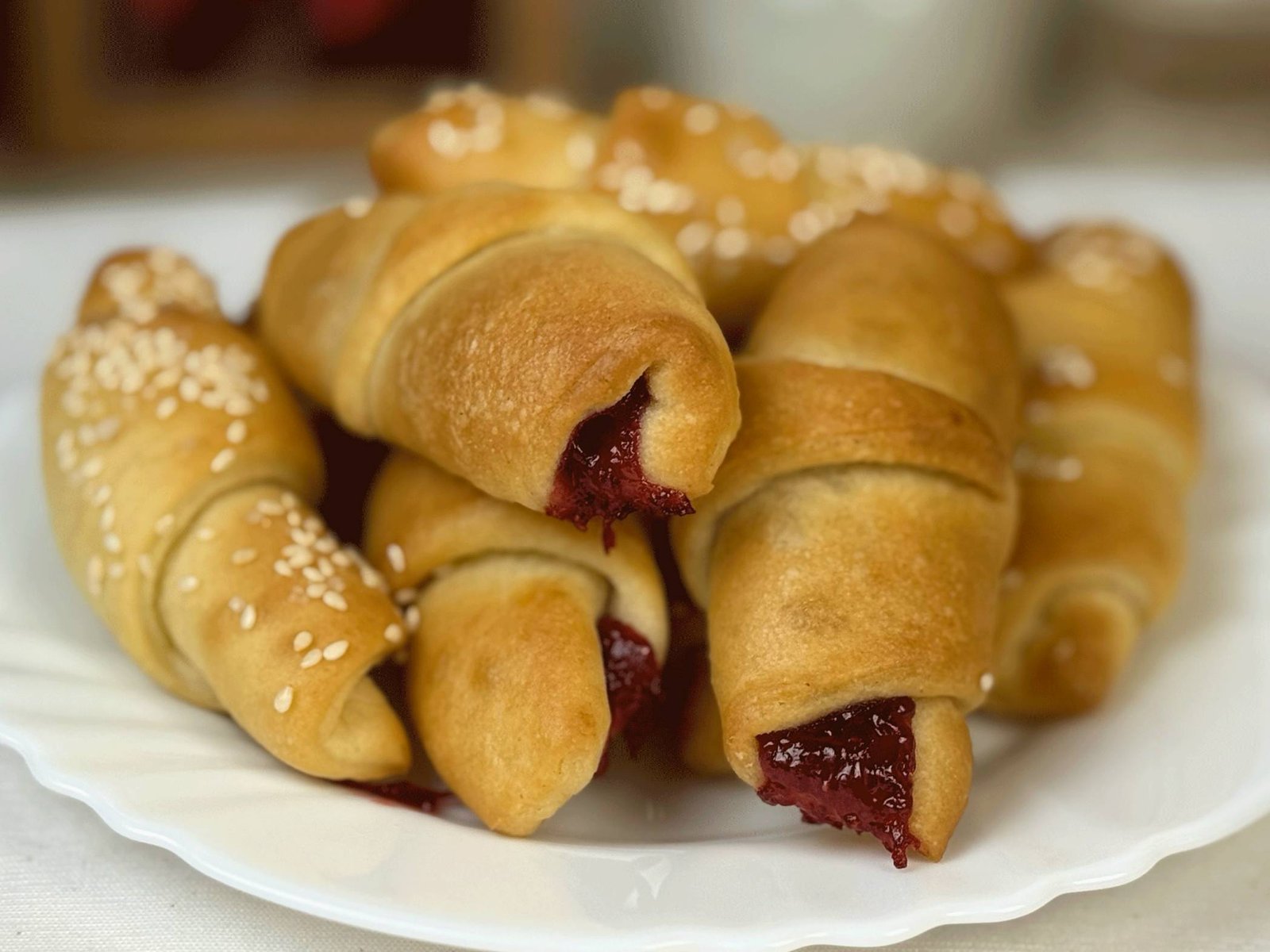 Gomila zlatno-žutih, mekanih posnih kiflica na bijelom tanjiru – miješane slane kiflice posute susamom i slatke kiflice punjene crvenim džemom.