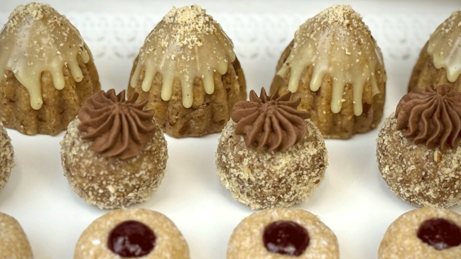 Servirani posni sitni kolači na bijeloj tacni, uključujući dekorativne jelkice sa bademom i bijelom čokoladom.