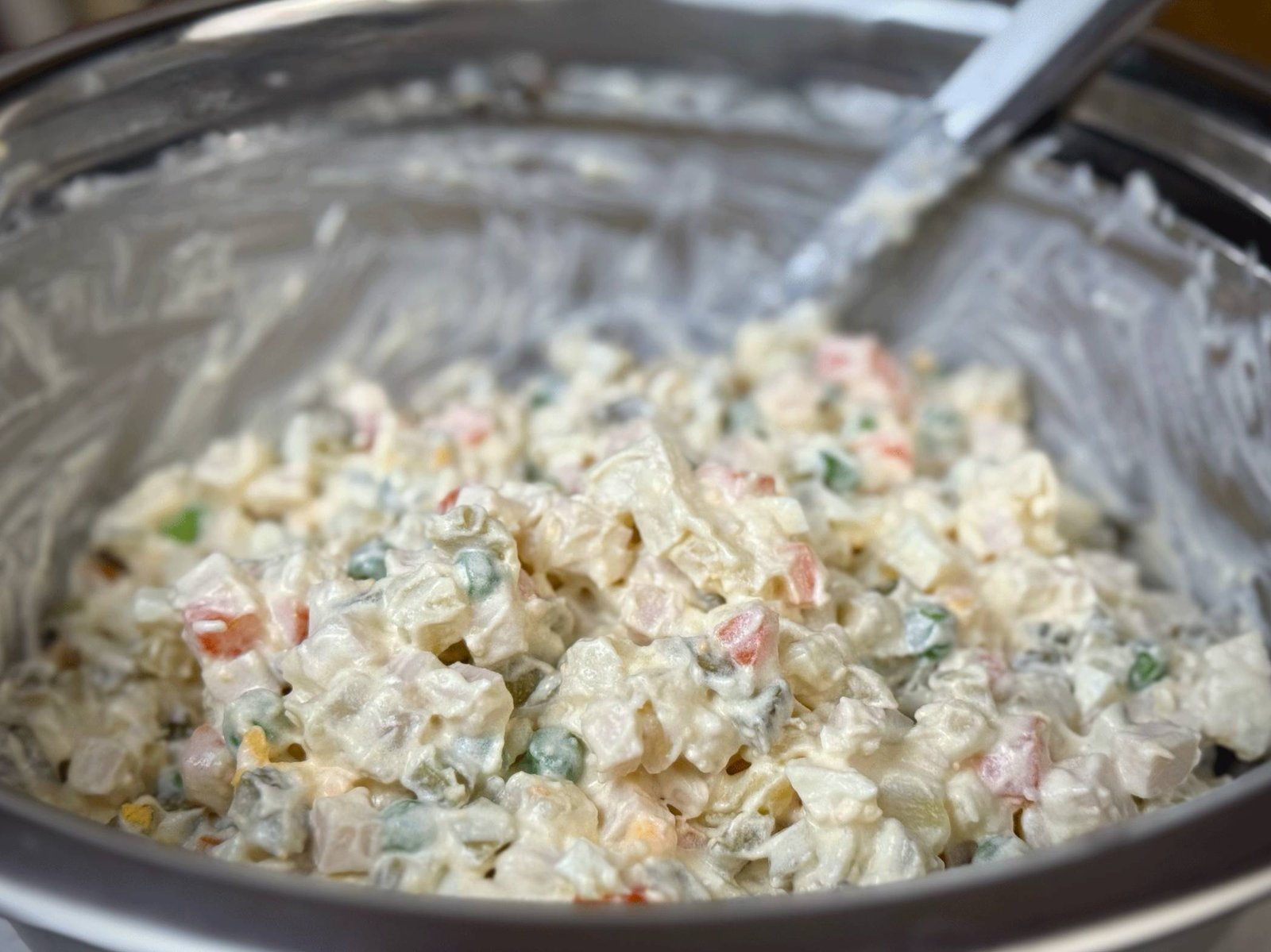 Svježe promiješana, kremasta ruska salata sjedinjena u velikoj metalnoj zdjeli sa kašikom za miješanje.