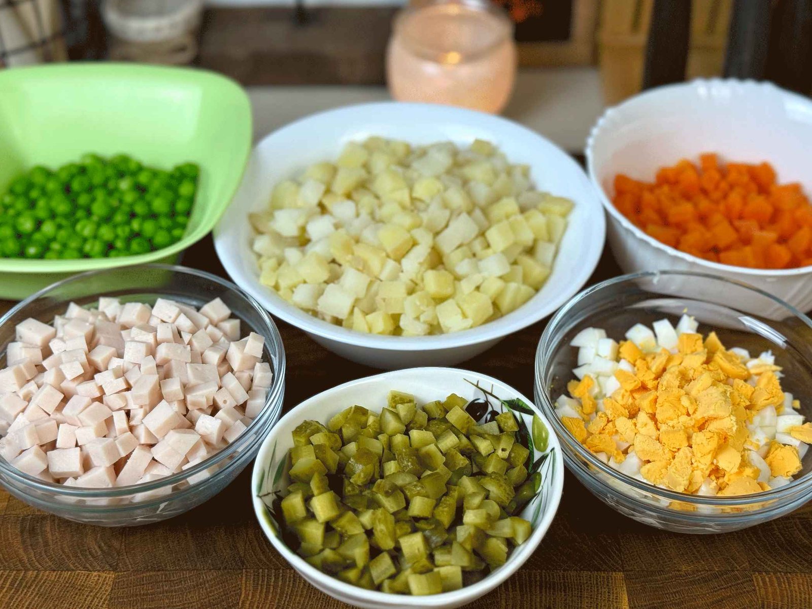 Sjeckani sastojci za rusku salatu (kockice krompira, mrkve, salame, jaja, krastavaca i grašak) raspoređeni u šest odvojenih zdjelica.