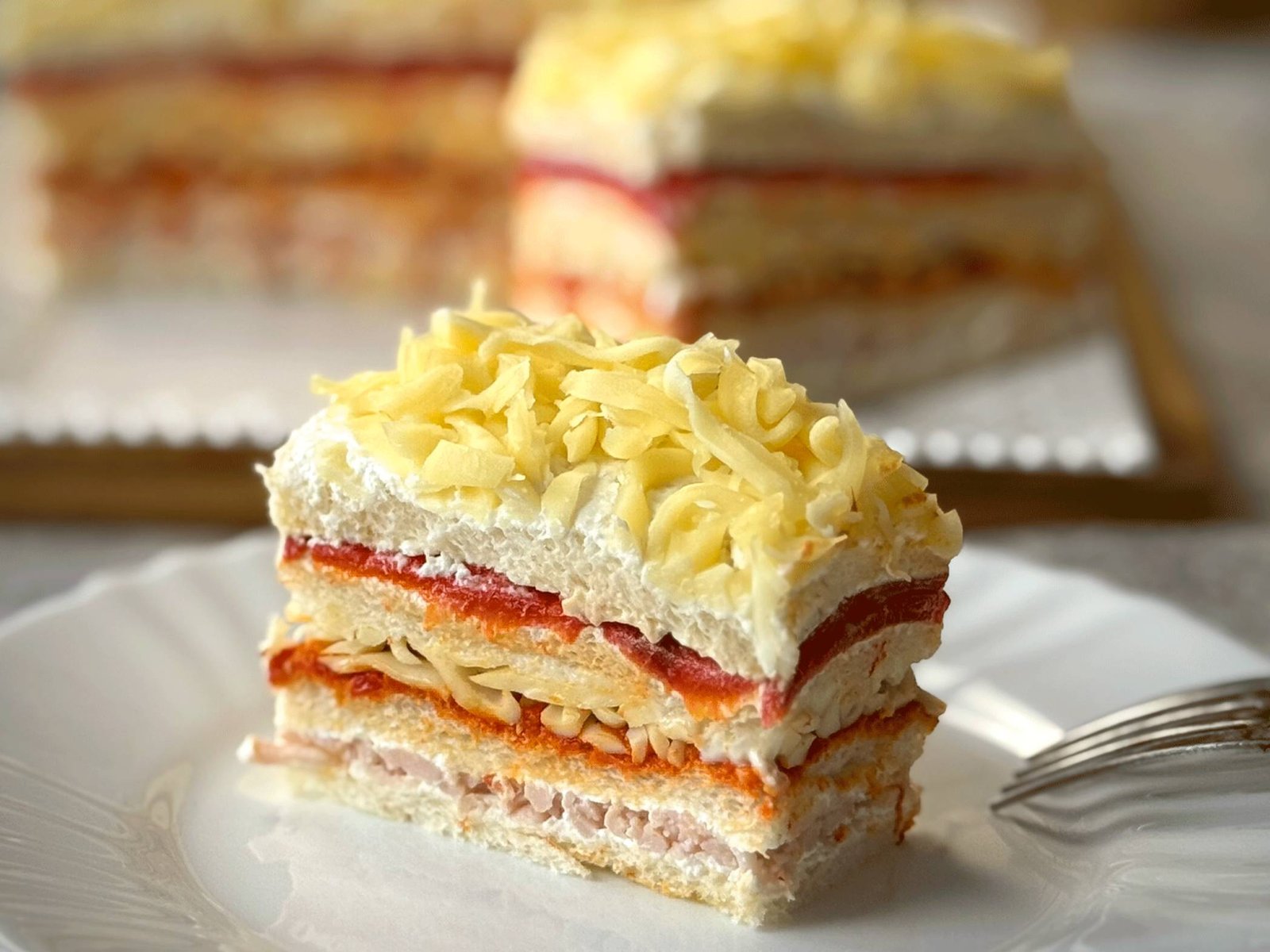 Servirano parče slane torte sa paprikama na bijelom tanjiru, sa vidljivim šarenim slojevima šunke, ajvara i sira.