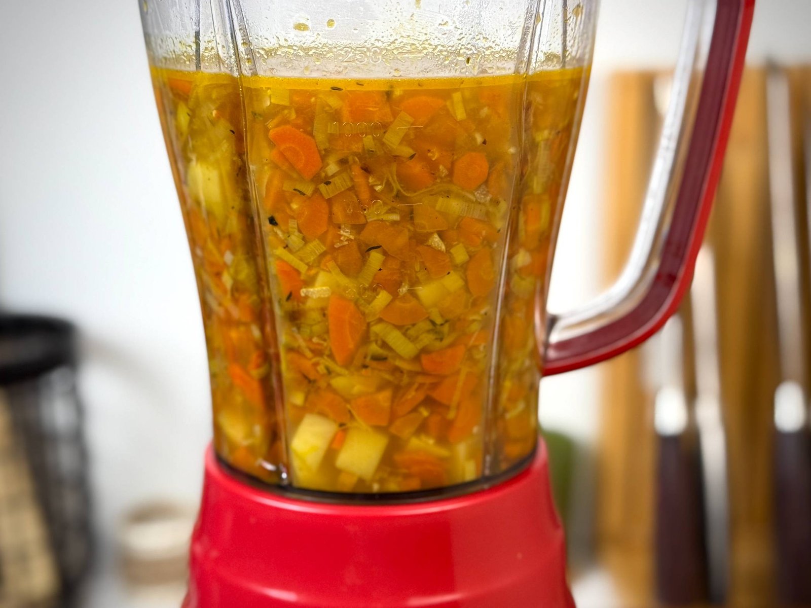 Povrće i temeljac u crvenom blenderu spremni za pretvaranje u kremasti potaž.
