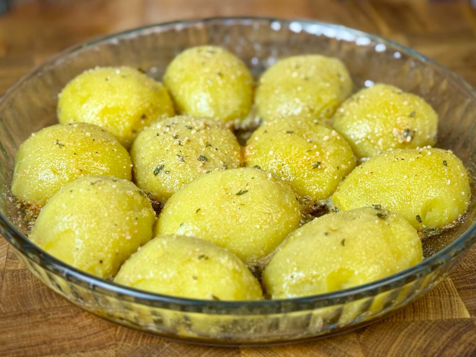 krompir-sa-parmezanom-prije-pecenja Oguljene polovine krompira poredane preko smjese sira i začina u vatrostalnoj posudi prije pečenja.