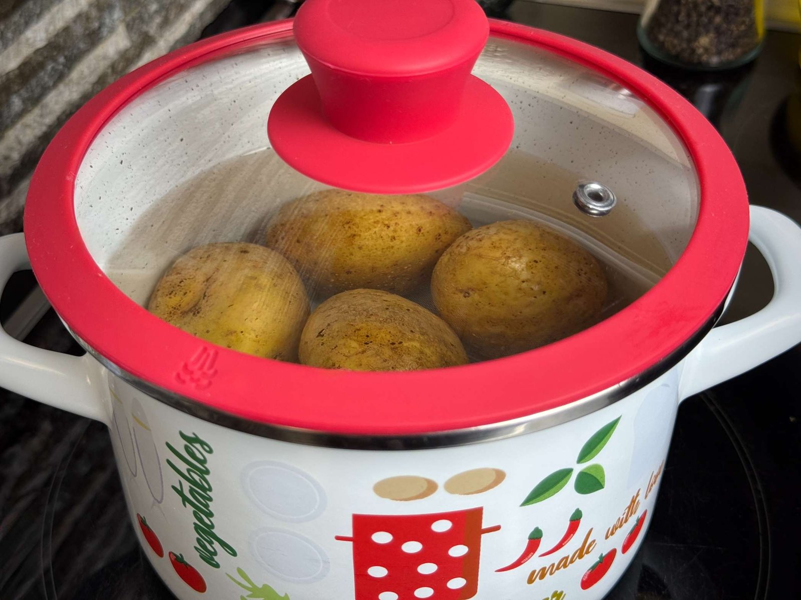 kuhanje-krompira-u-ljusci Krompir koji se kuha u šerpi sa vodom pod zatvorenim crvenim poklopcem.