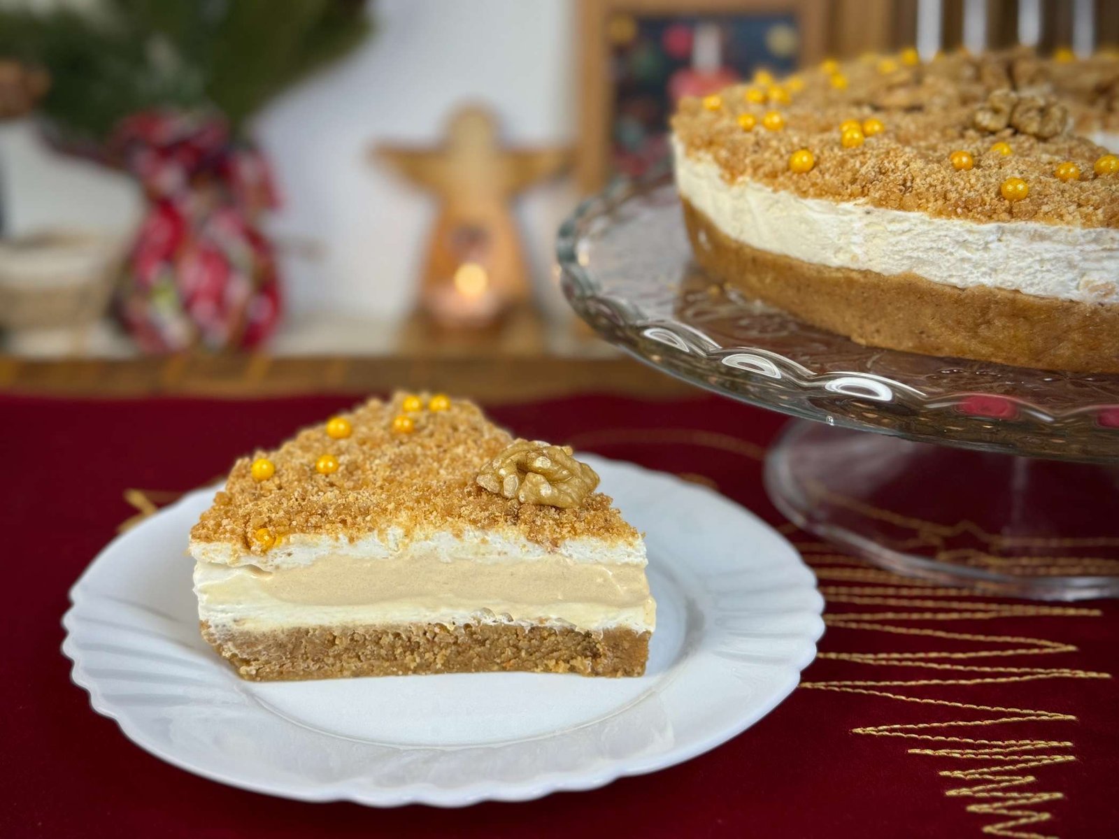 Parče Medena Plazma kolača na tanjiru sa dekoracijom od pečenih oraha i žutih perlica, servirano uz cijelu tortu na stalku.