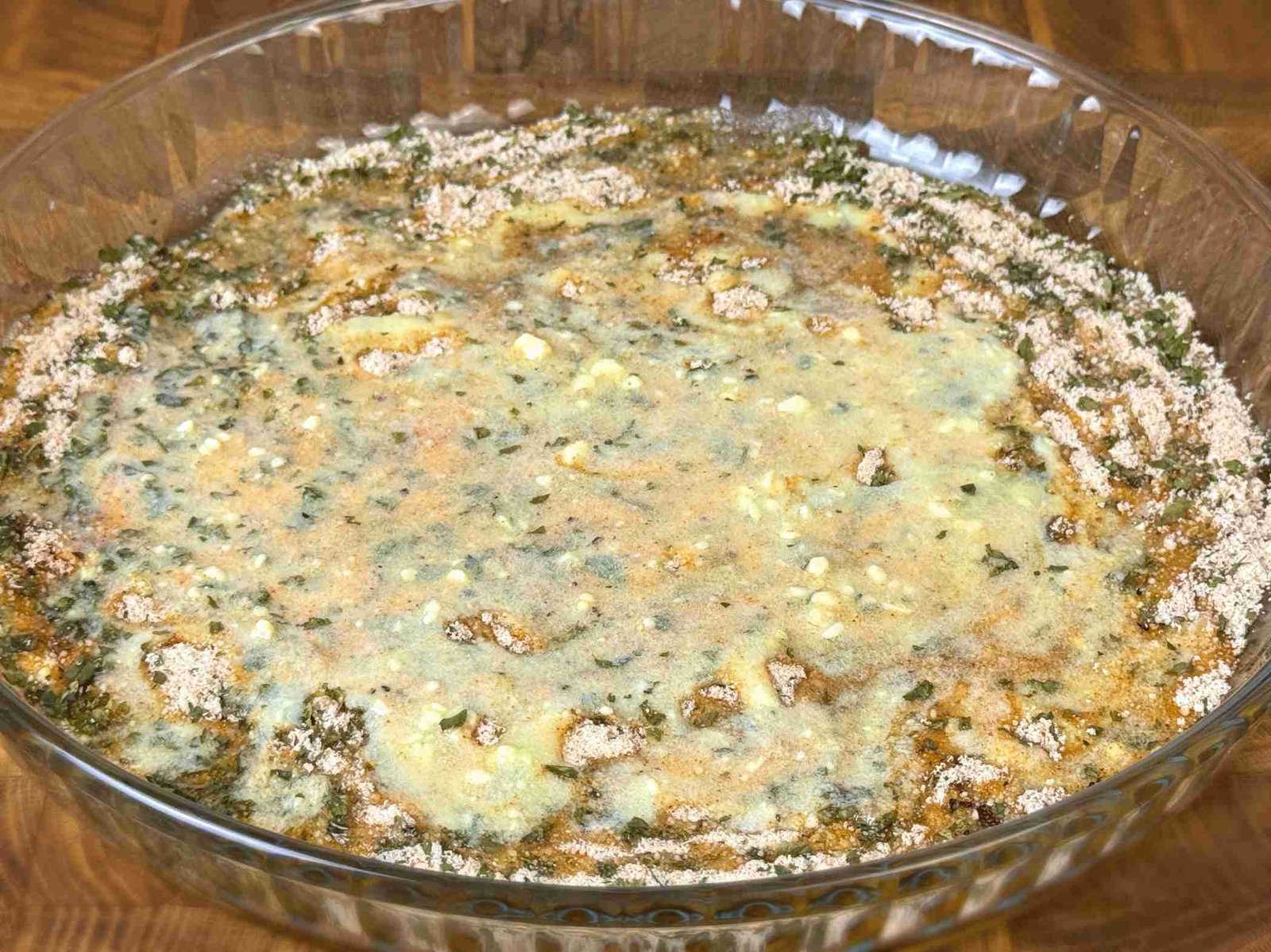 priprema-parmezana-i-zacina-u-plehu Stakleni pleh sa ravnomjerno raspoređenim parmezanom, maslacem i začinskim biljem.