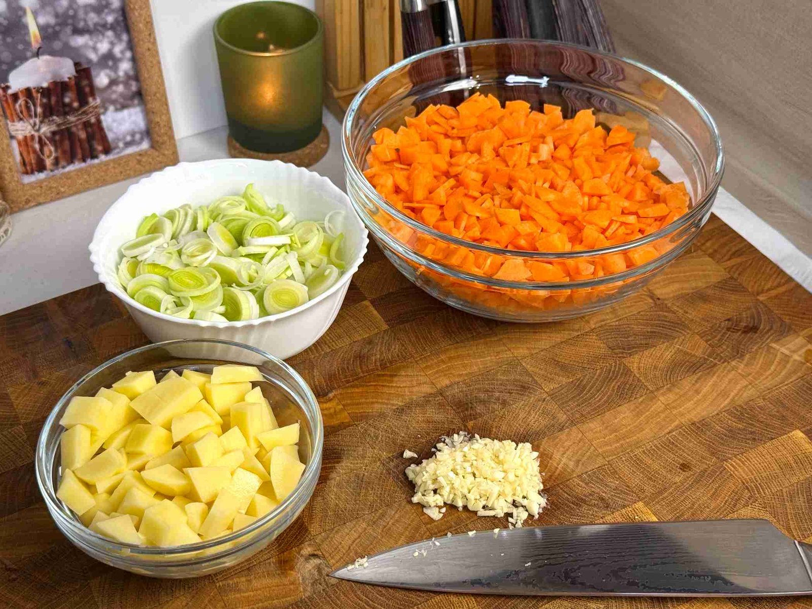 Isjeckana mrkva, praziluk, krompir i bijeli luk u staklenim zdjelicama na drvenoj dasci.