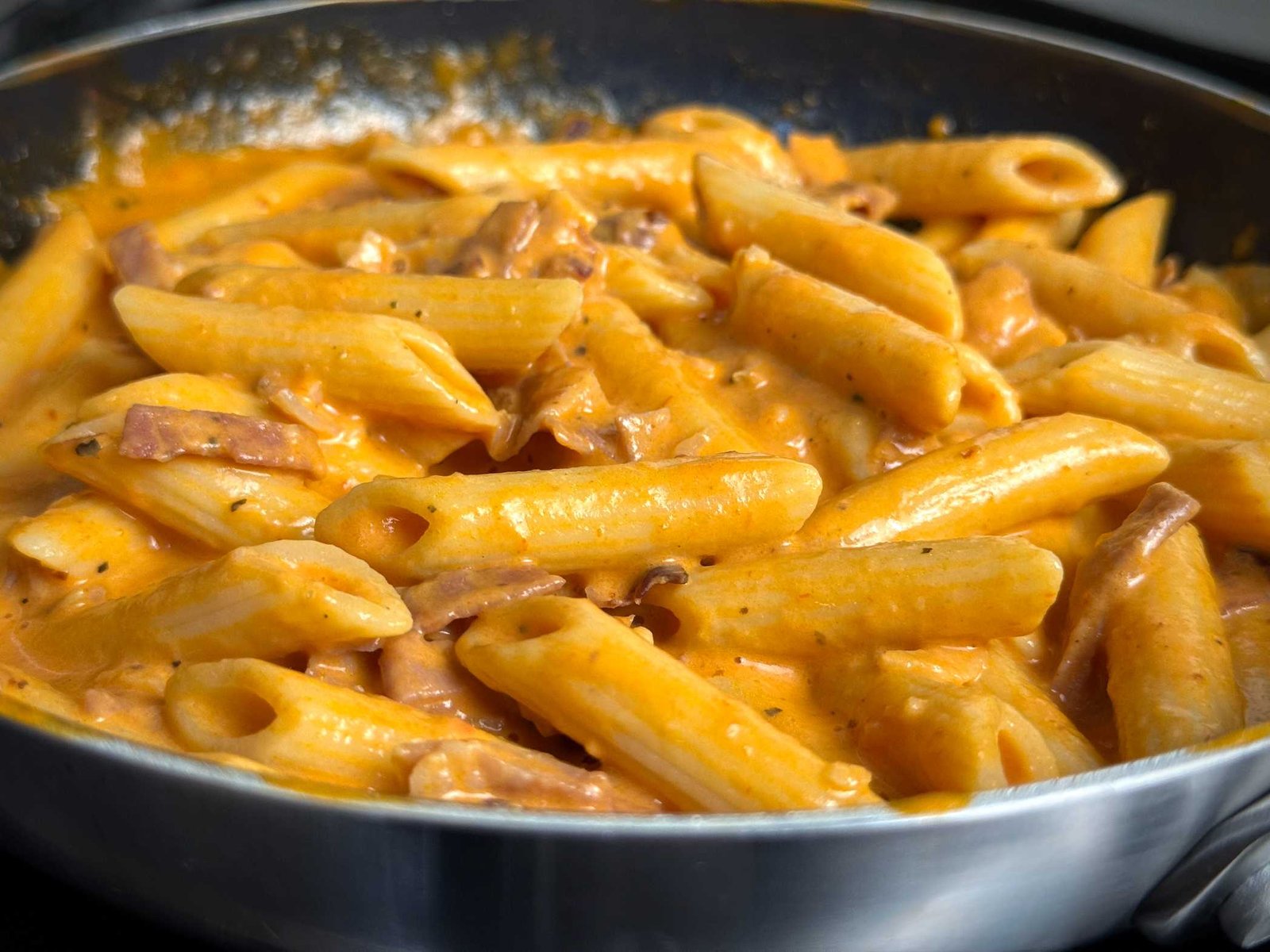 Penne tjestenina sjedinjena sa bogatim, kremastim narandžastim sosom u tavi.