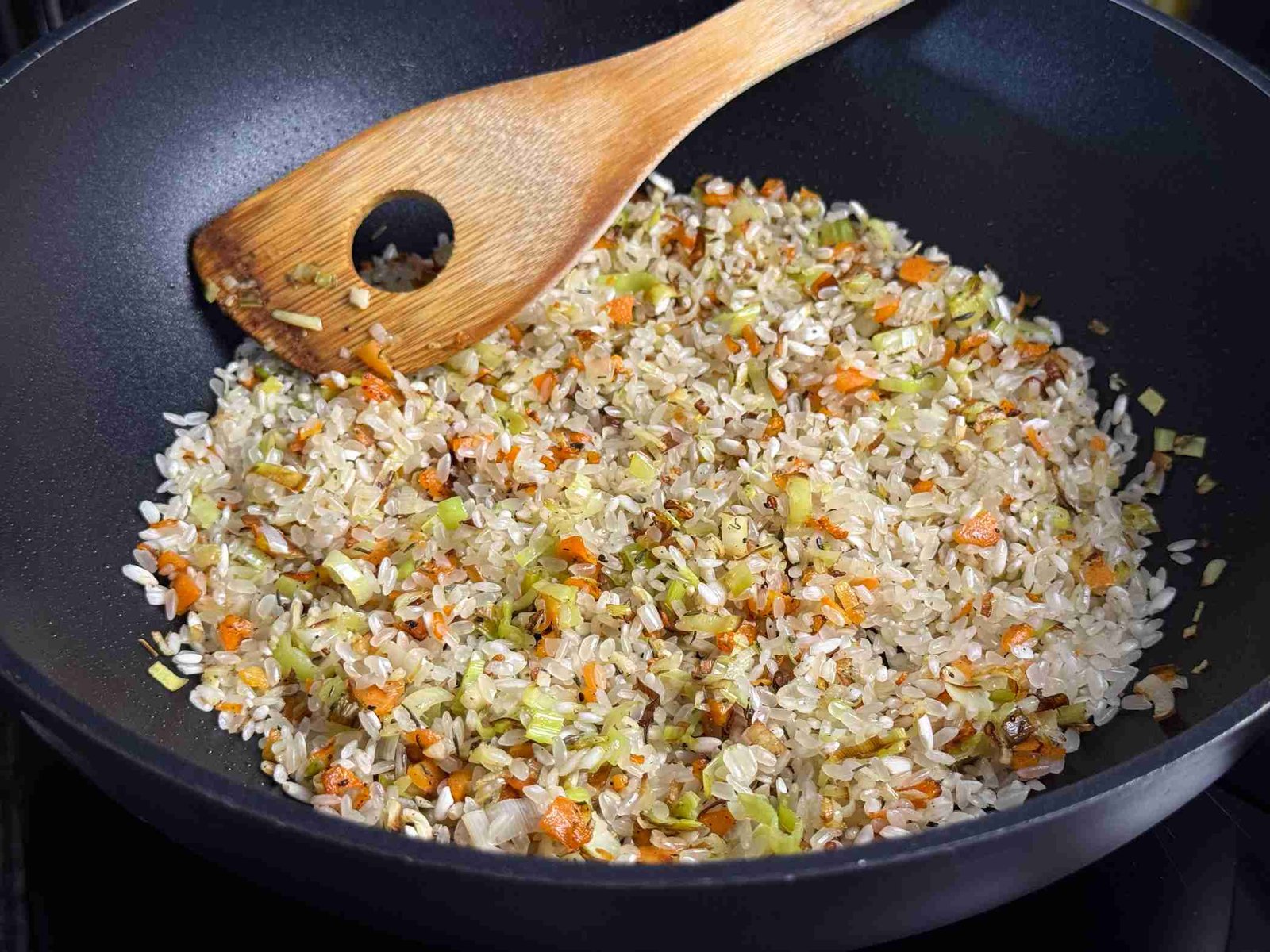 Prženje isjeckanog praziluka, mrkve i riže u tavi na ulju.