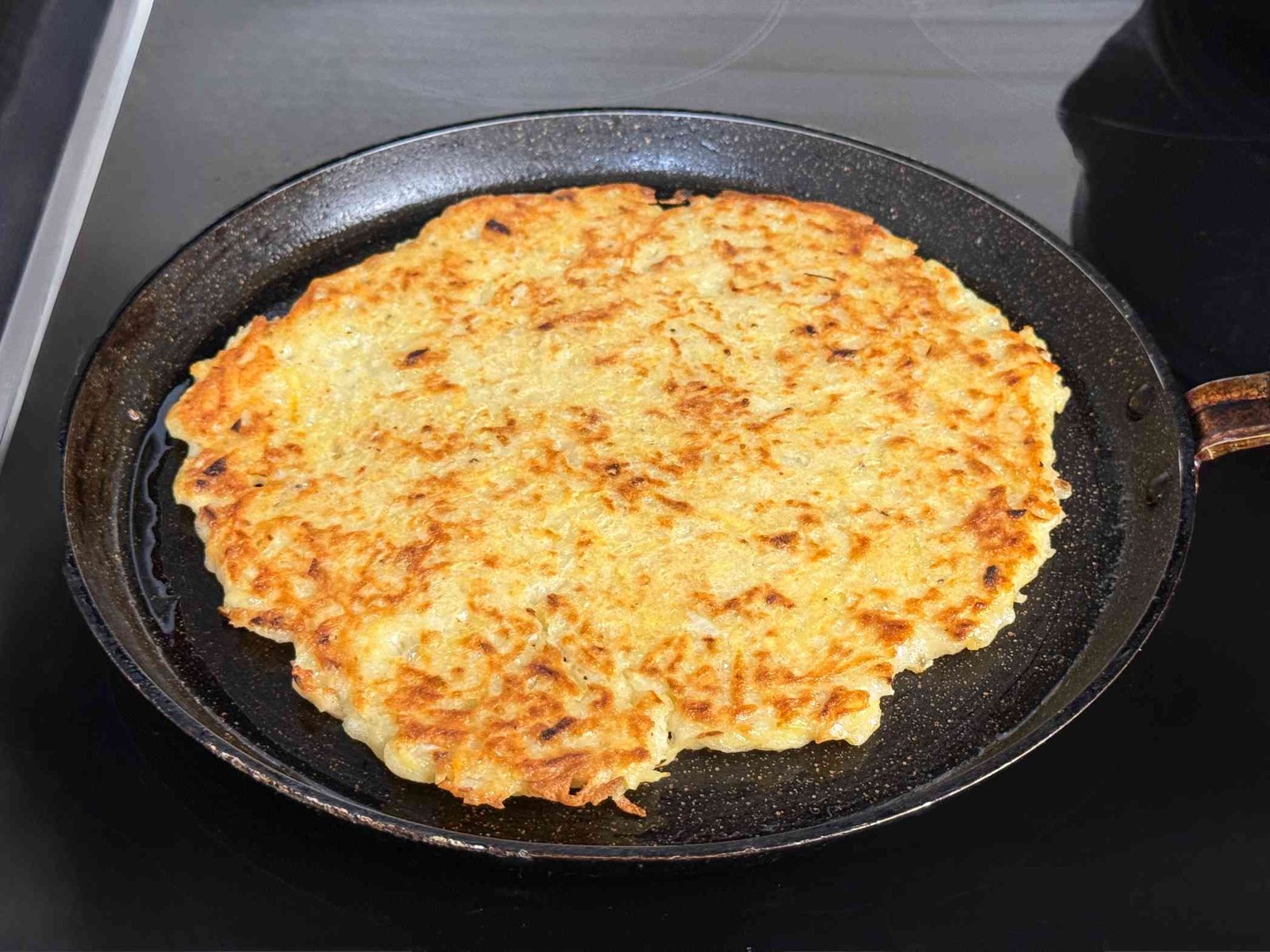 Velika palačinka od rendanog krompira pržena u tavi .