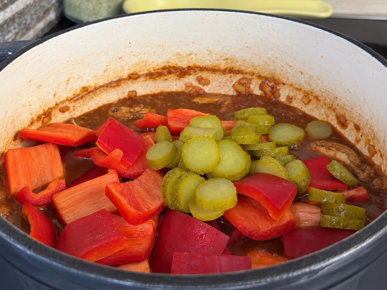 Crvena paprika i kiseli krastavci dodani u gulaš tokom pripreme.