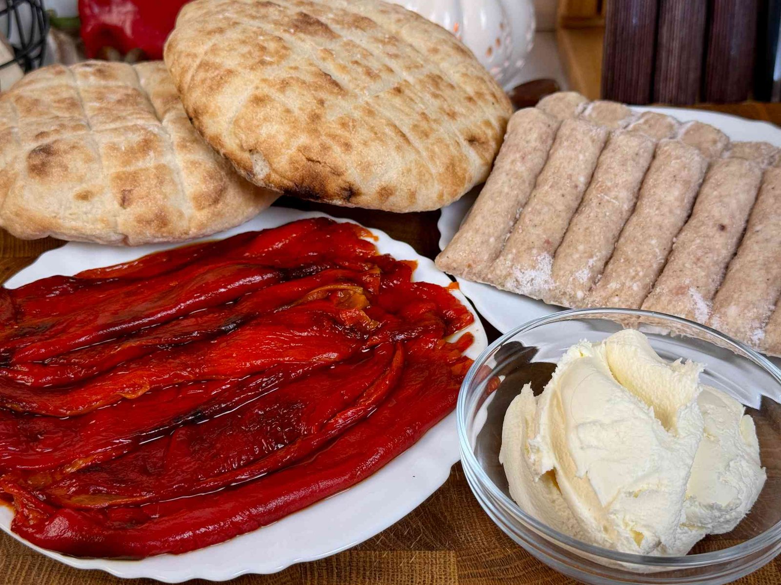 sastojci-za-cevape-sa-kajmakom-i-paprikom Ćevapi, pečene crvene paprike, kajmak i lepinje pripremljeni za pravljenje brzog ručka.