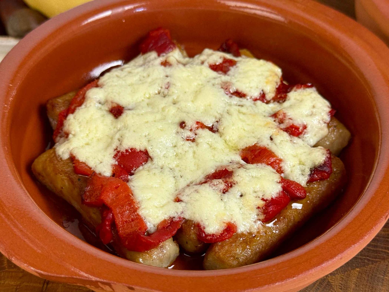 zapeceni-cevapi-sa-kajmakom-i-paprikom Zapečeni ćevapi sa crvenim paprikama i rastopljenim kajmakom u keramičkoj posudi.